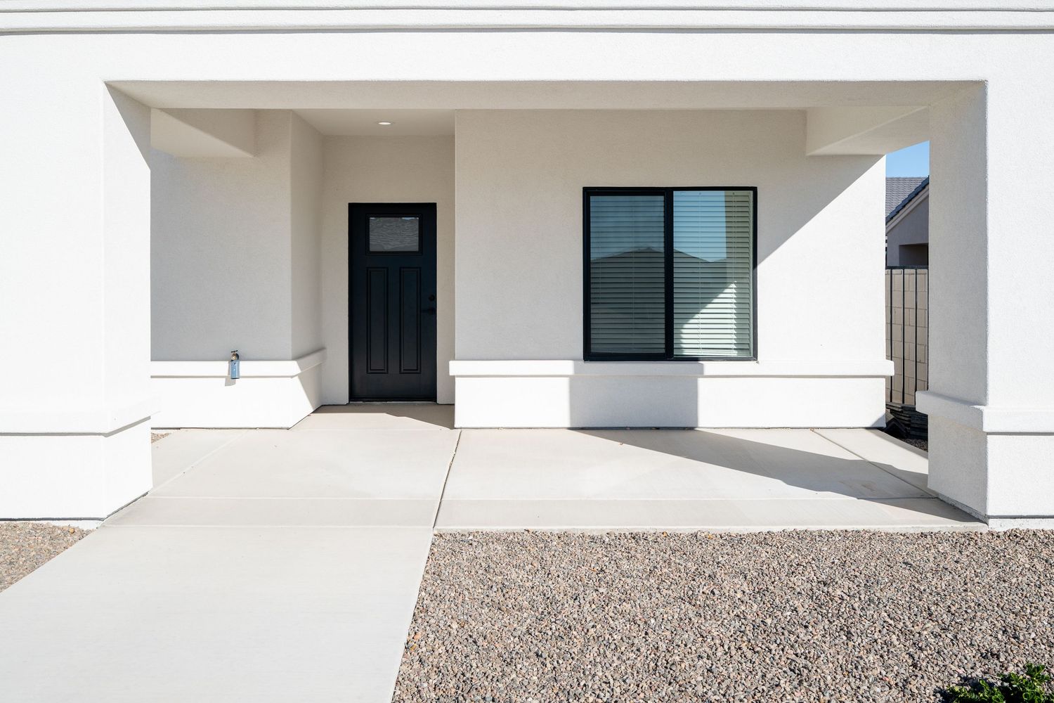 Modern white house exterior with gravel landscaping and clean architectural lines against a bright sky.