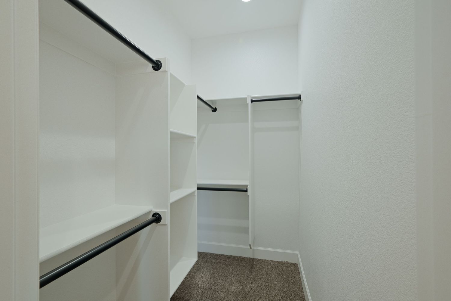 A long white walk-in closet with black hanging rods and bright lighting installed along the walls.