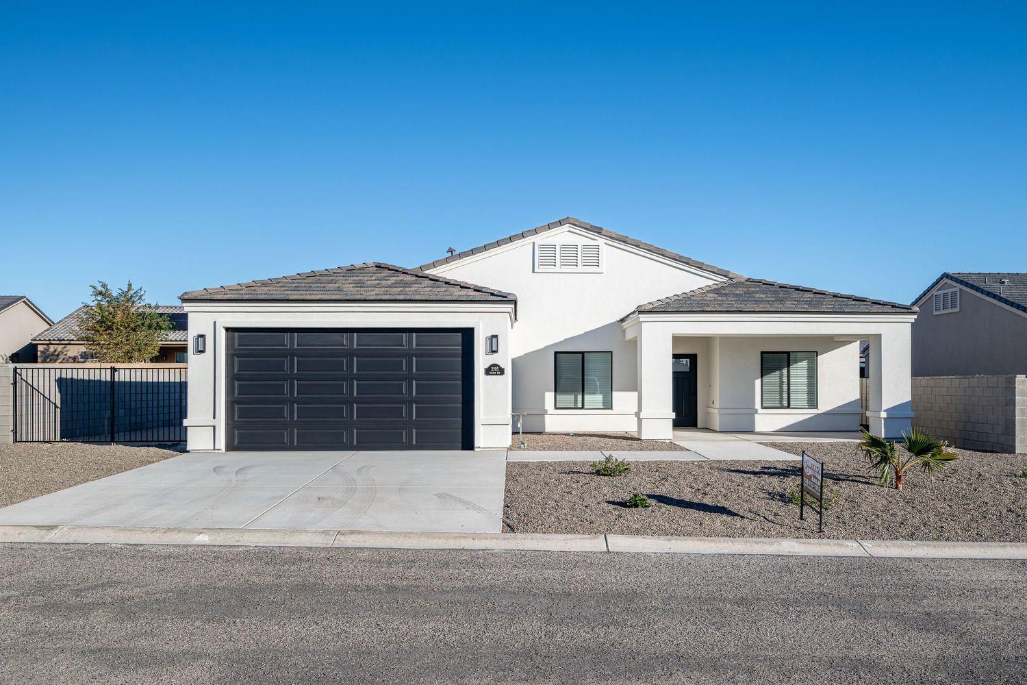 Modern single-story house with white exterior, two-car garage and desert landscaping under bright blue sky.