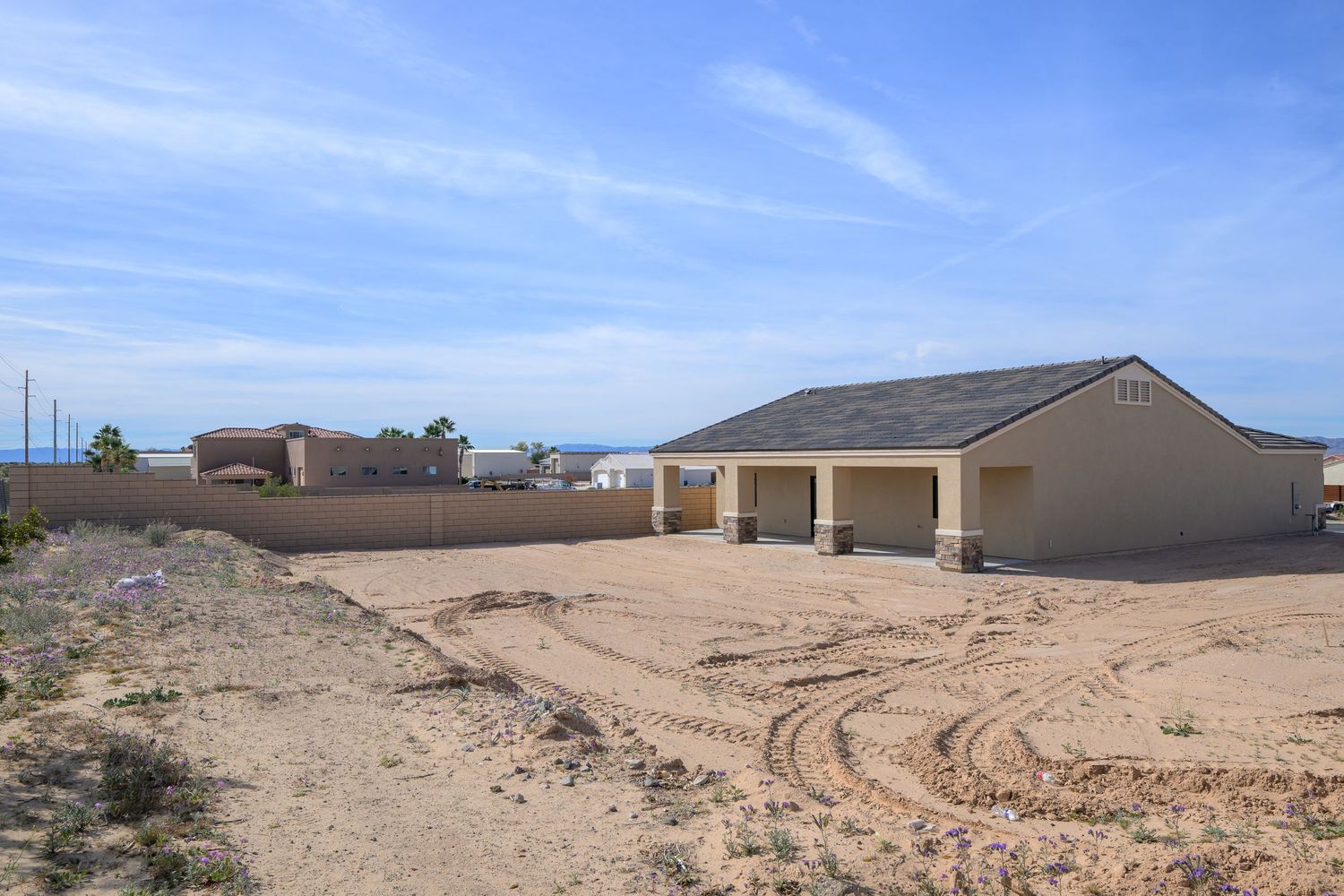 Desert landscape with residential construction site and scattered buildings under bright blue sky.