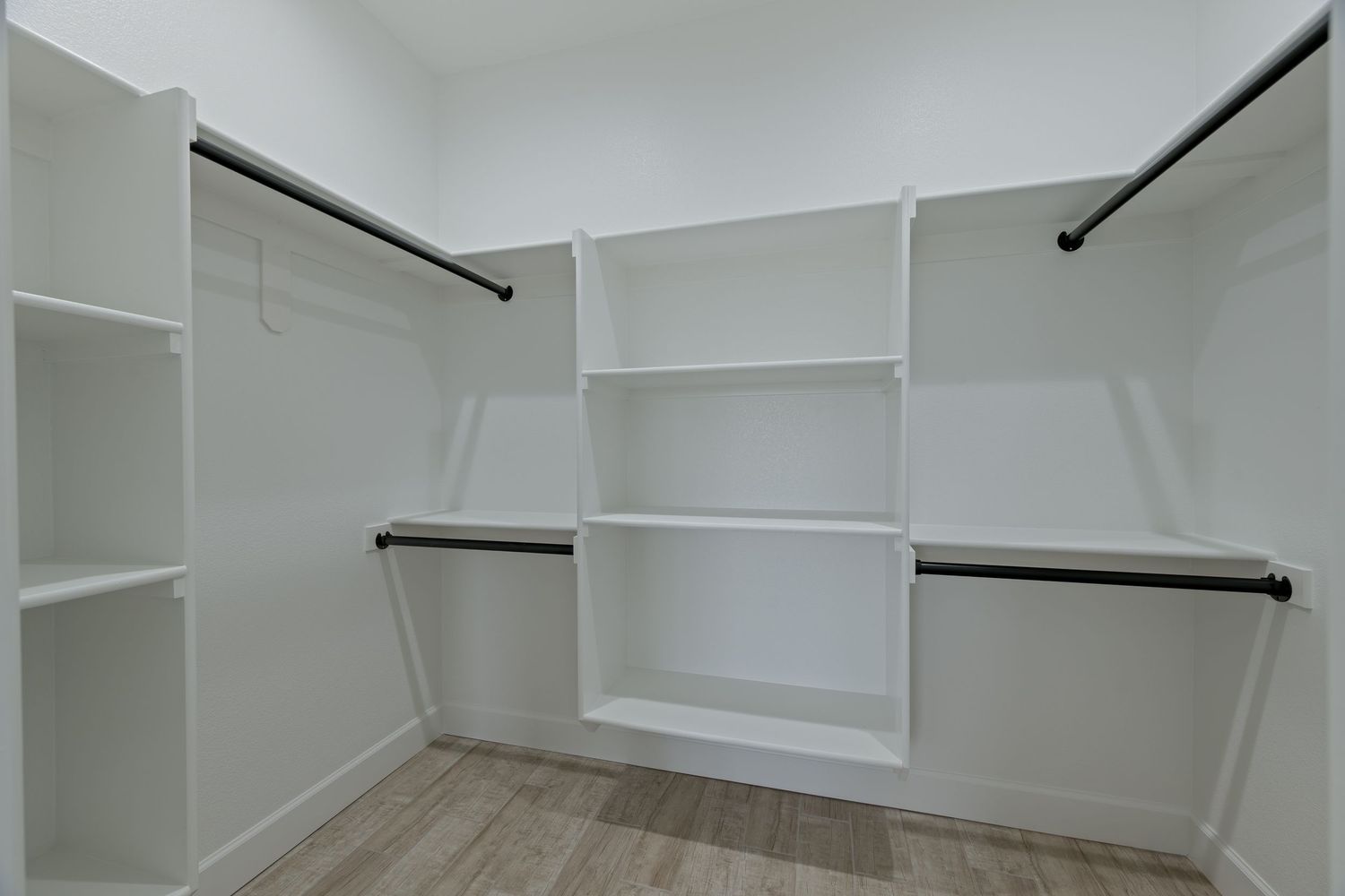 Spacious walk-in closet with white built-in shelving, double hanging rods, and light wood flooring.