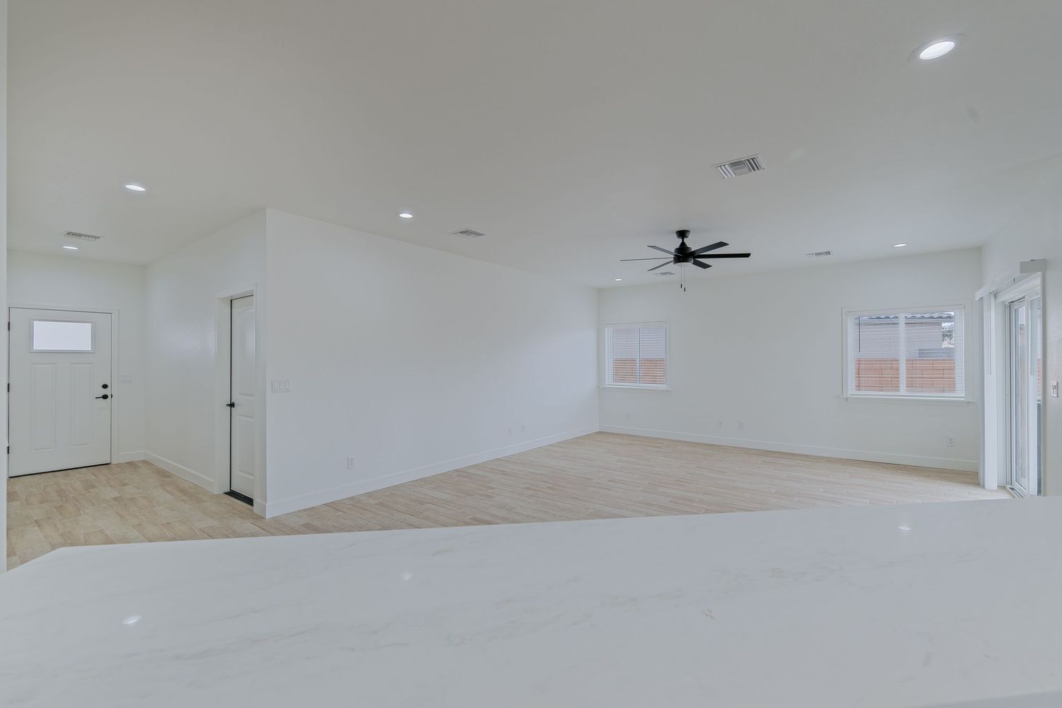 Bright open living room with white walls, light tile flooring, recessed lighting, and a black ceiling fan.
