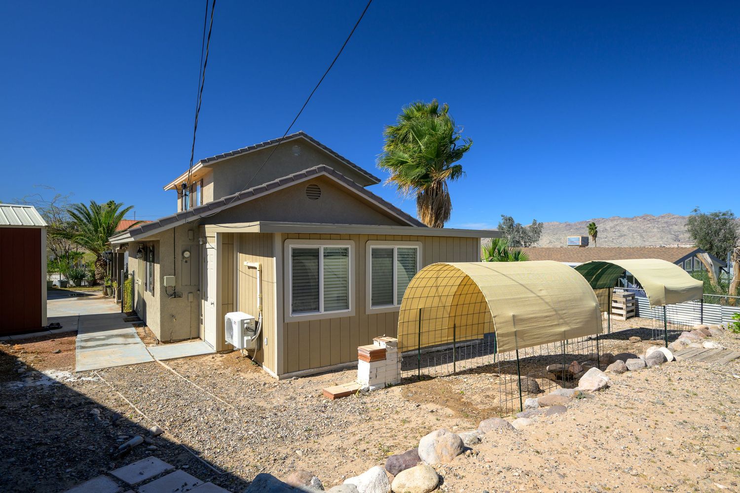 Desert landscape with single-story residential homes and rocky terrain under bright blue sky.
