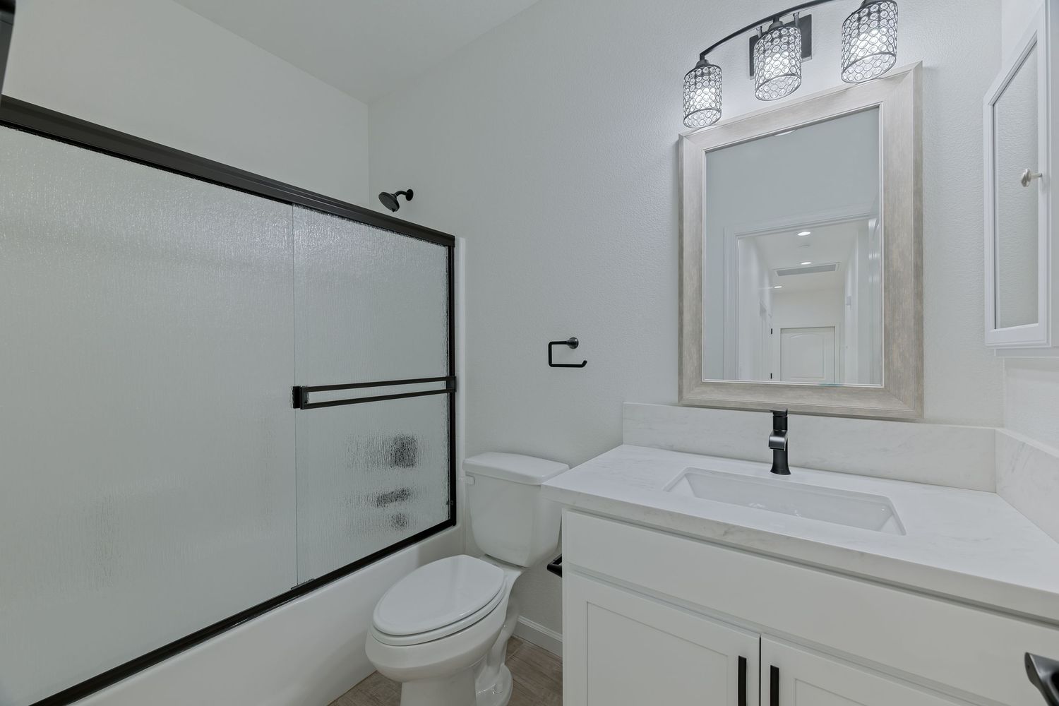Modern bathroom with sliding glass shower door, white vanity, framed mirror, and toilet in a bright, clean space.
