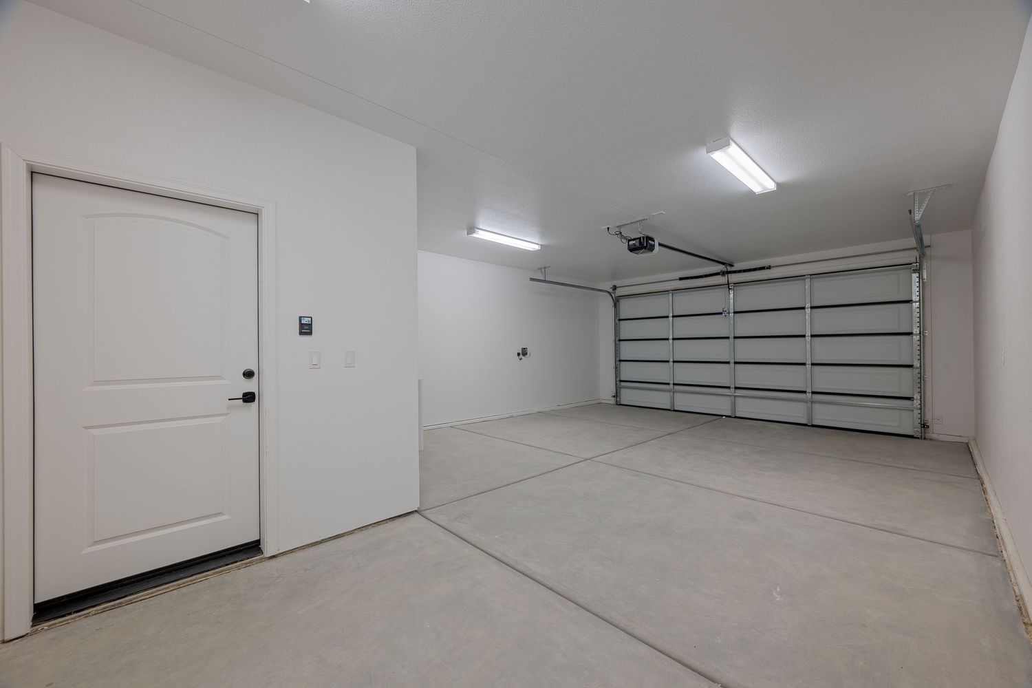 Interior view of a modern storage facility hallway with white walls, concrete floor, and fluorescent lighting.