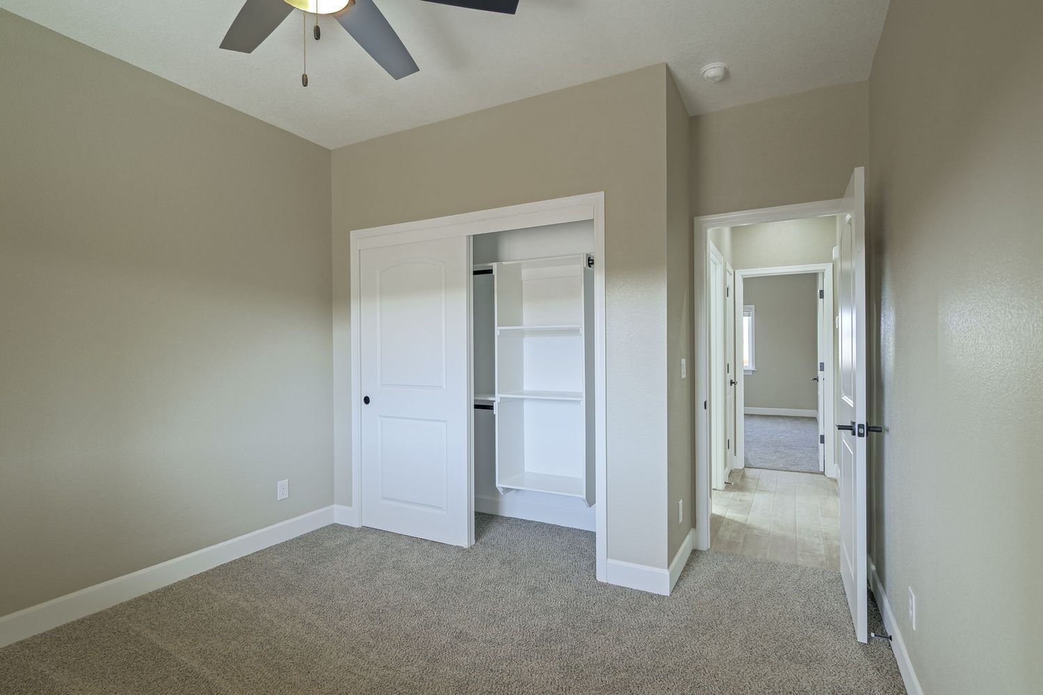 Interior view of an empty room with beige walls, white trim, and ceiling fan showing multiple doorways and natural light.
