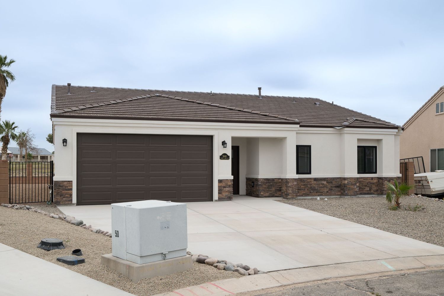 Single-story desert home with brown garage door, stone accents, and concrete driveway in a sunny Southwest neighborhood.