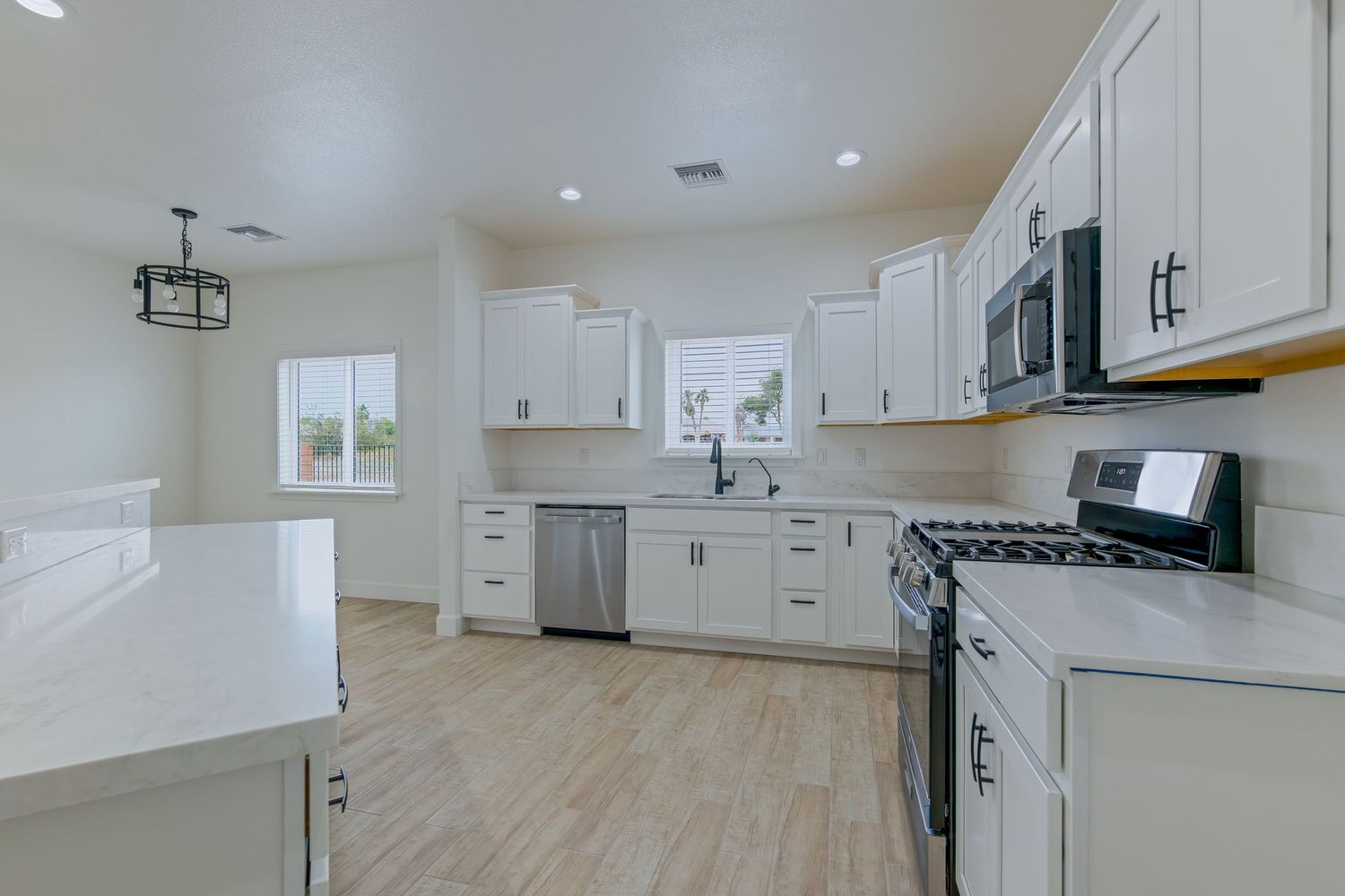 Modern kitchen with white cabinets, stainless steel appliances, quartz countertops, and light hardwood floors.