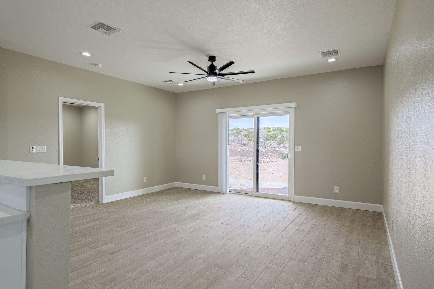 Panoramic view of an empty living area with ceiling fan, recessed lighting, and large windows bringing in natural light.