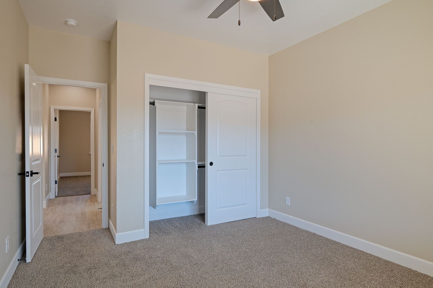 Unfurnished bedroom with beige walls, white trim, carpet flooring and built-in closet with double doors.