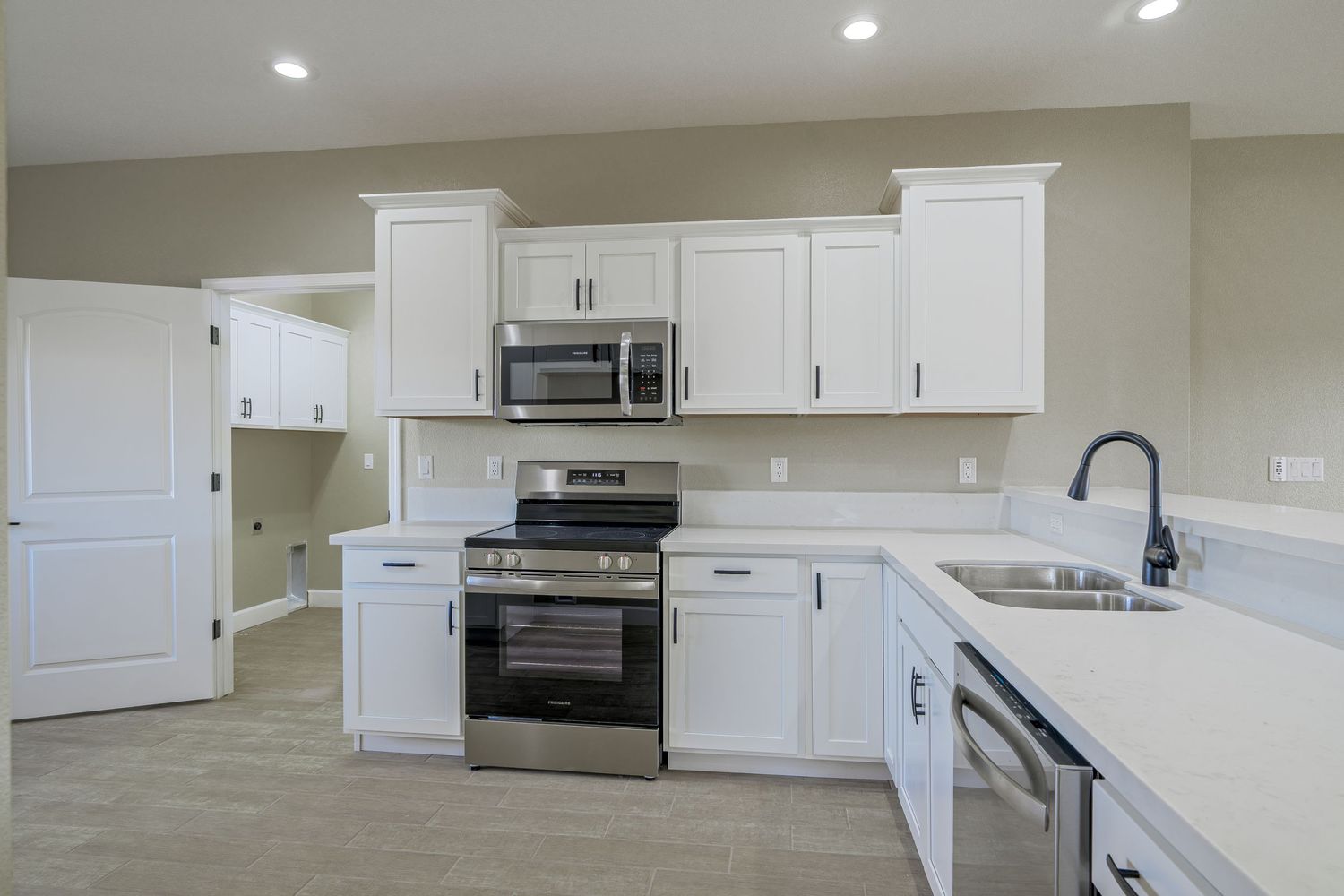 Modern white kitchen with stainless steel appliances, quartz countertops, and recessed lighting in a new construction home.