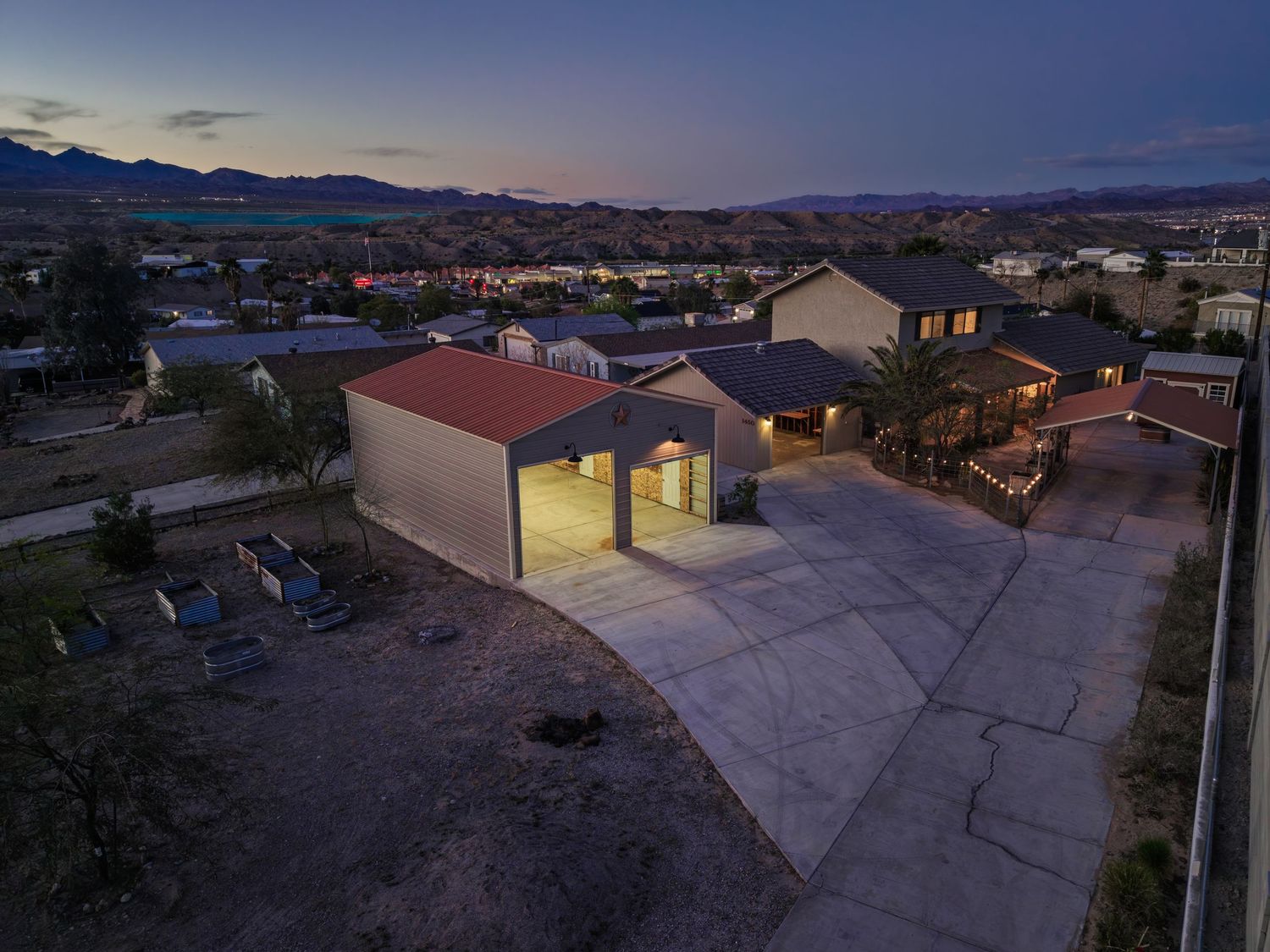 Aerial panoramic view of desert mountains and residential buildings at dusk with glowing lights in the distance.