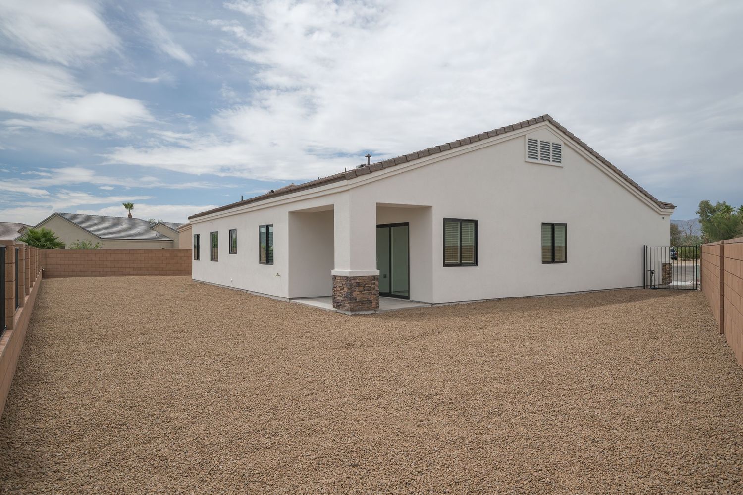 Rear exterior of a white stucco single-story home with gravel yard, green-trimmed windows, and covered patio area.