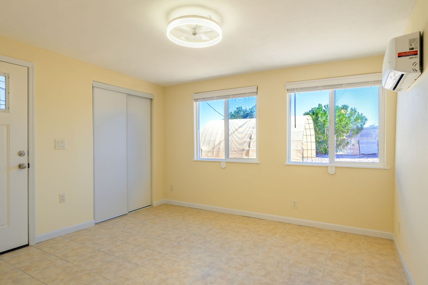 A bright, empty interior room with beige carpeting, white walls, and natural light streaming through multiple windows.