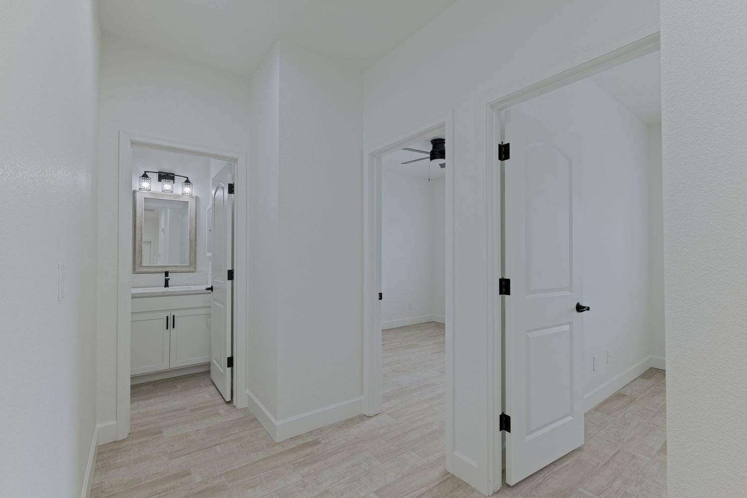 Bright white hallway with light wood floors, open doors leading to a bathroom with vanity and a closet.