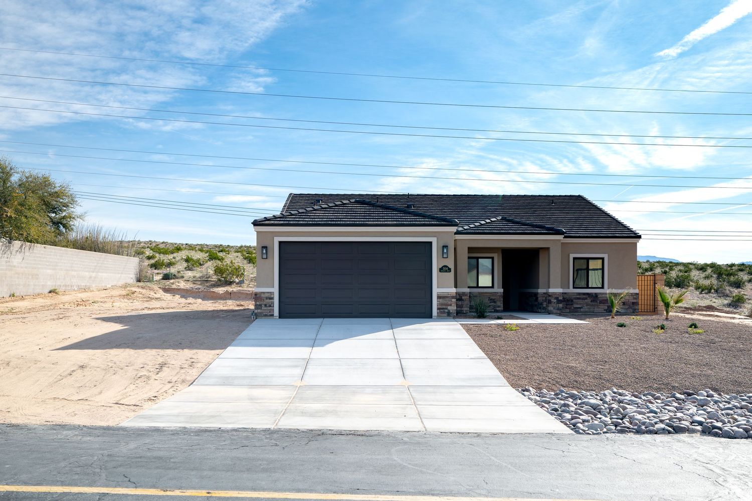 Modern single-story home with concrete driveway and desert landscaping under bright blue sky.