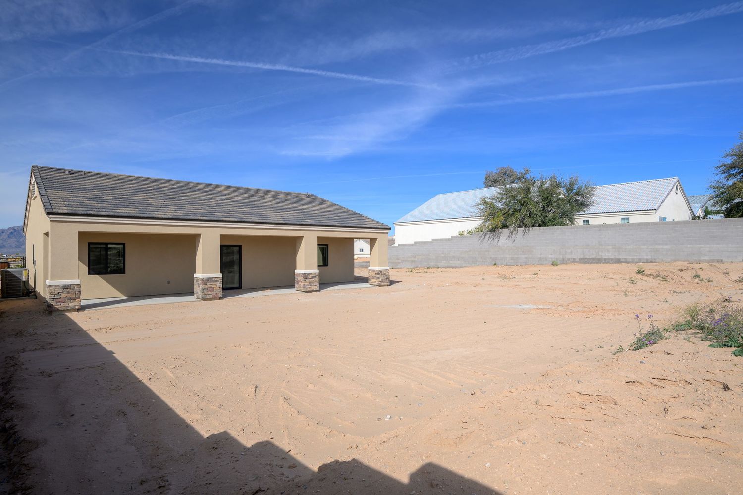 Desert landscape with scattered residential buildings and sandy terrain under bright blue sky.