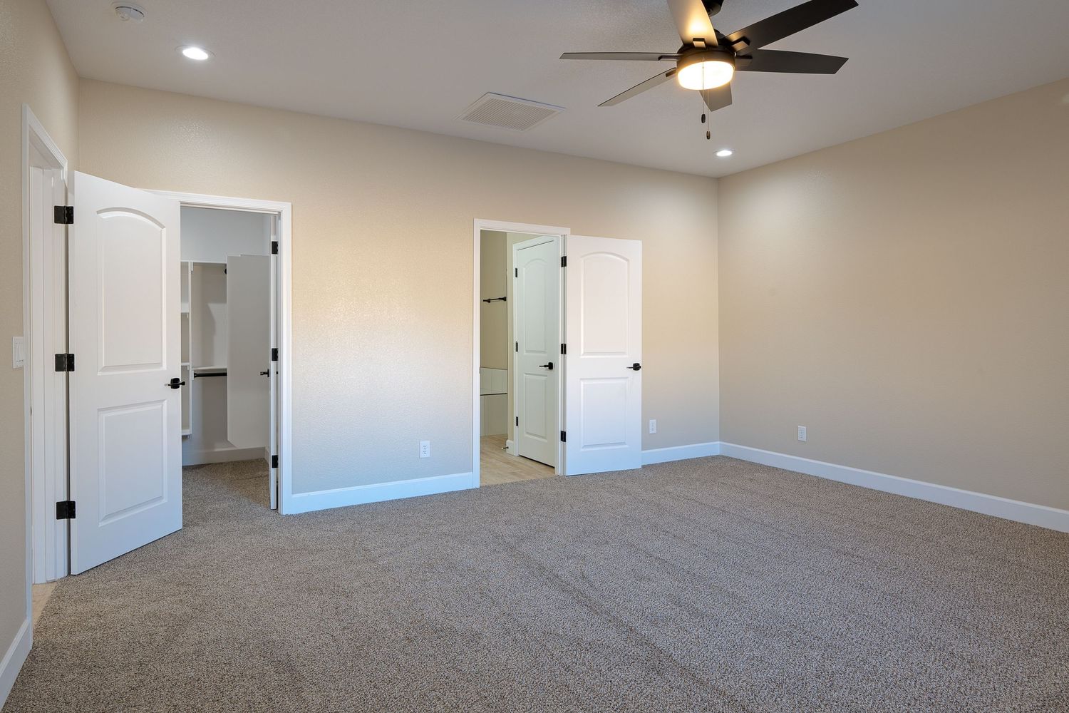 Empty bedroom with beige walls, brown carpet, ceiling fan, and two white doors showing a clean modern interior design.