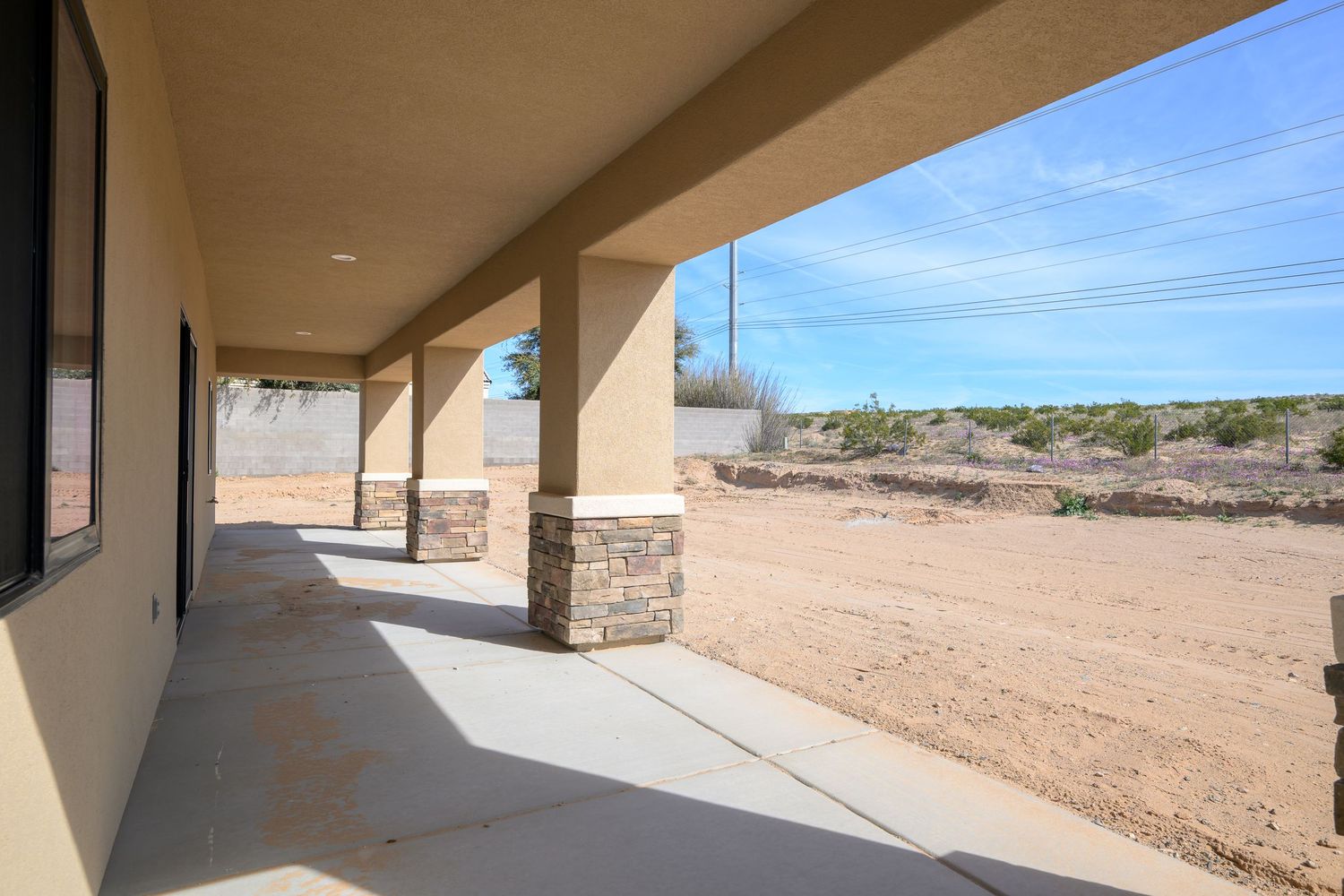 A modern stucco home with a covered patio and desert landscaping stands against a bright blue sky.