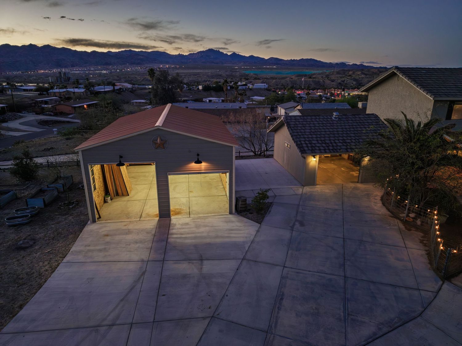 Panoramic sunset view of a desert property with illuminated buildings and mountains silhouetted against the sky.