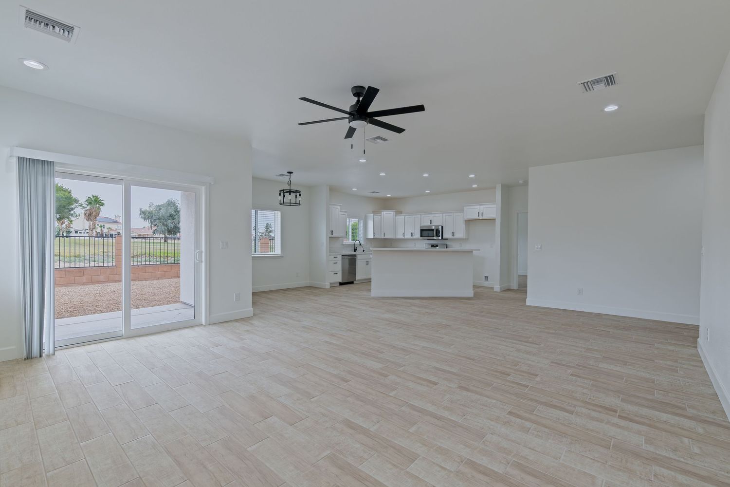 Spacious open-concept living room with light wood floors, ceiling fan, and modern kitchen visible in the background.
