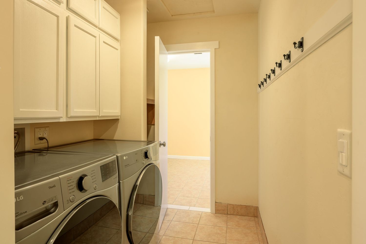 A modern laundry room with white cabinets, washer and dryer units, and cream-colored walls.