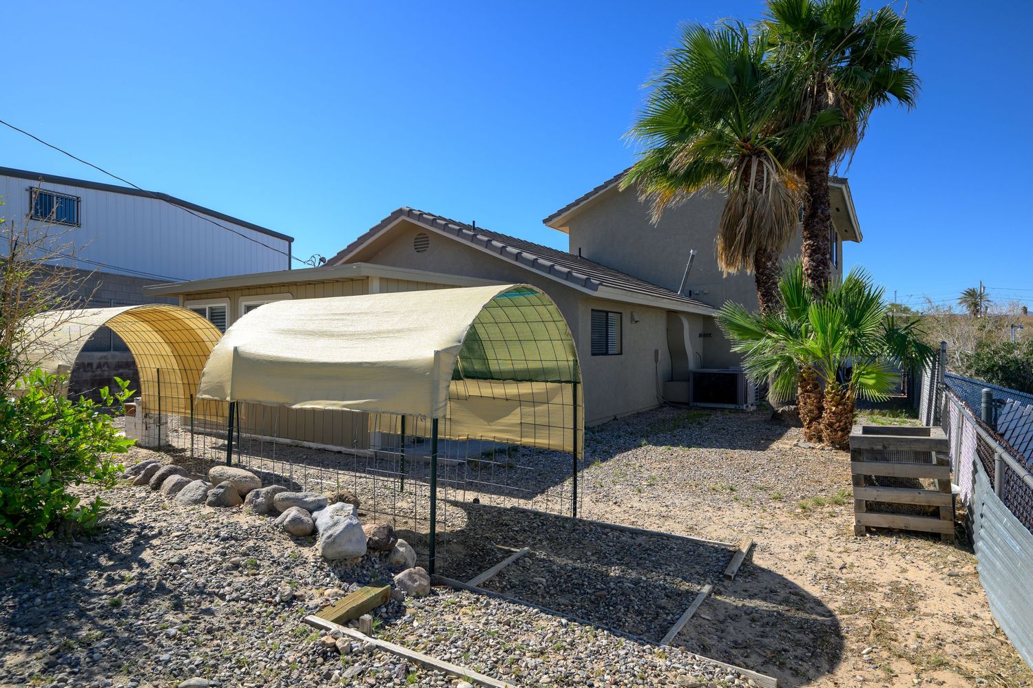 Panoramic view of desert landscaping with palm trees, gravel, and residential homes under bright blue sky.
