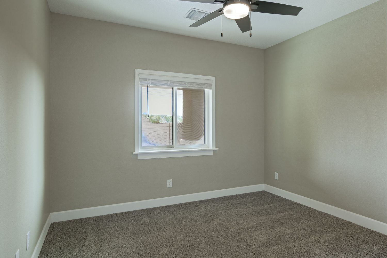 Spacious empty bedroom with beige walls, ceiling fan, and small window showcasing natural light.