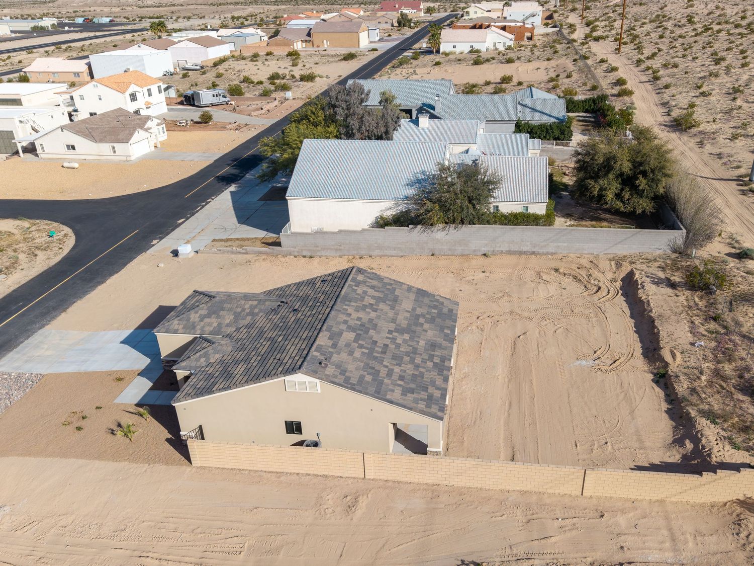 Aerial view of desert property with metal buildings and paved roads in a rural residential area.