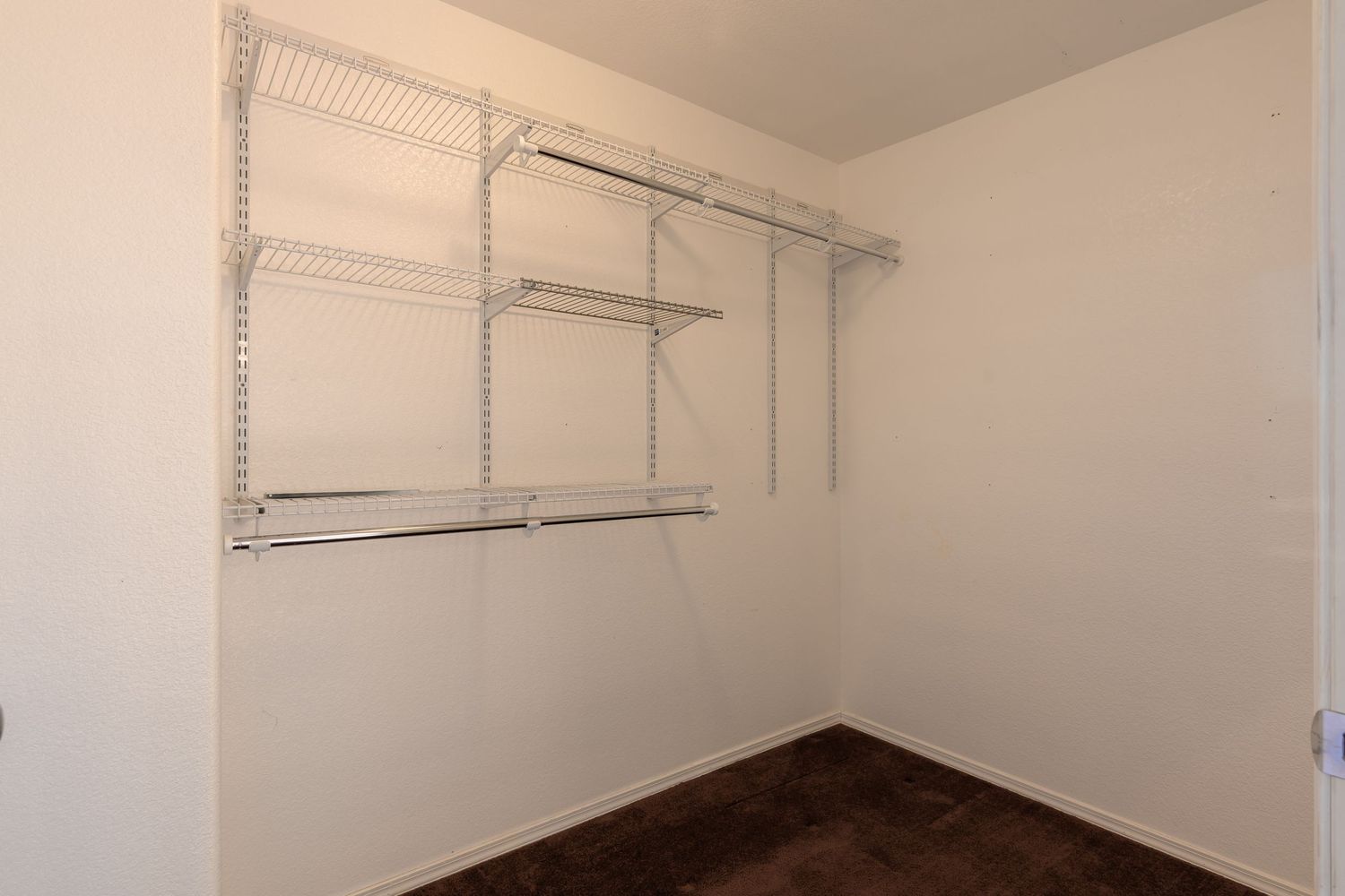 Empty white walk-in closet with metal hanging rods and shelving mounted on walls.