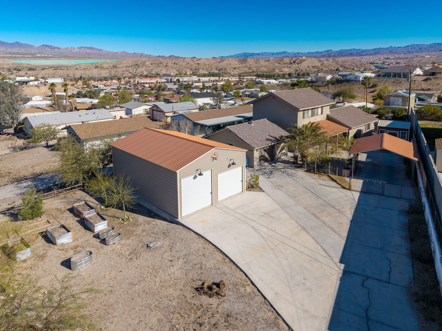 Aerial drone view of desert residential property with brown roof and white walls surrounded by arid terrain and mountains.