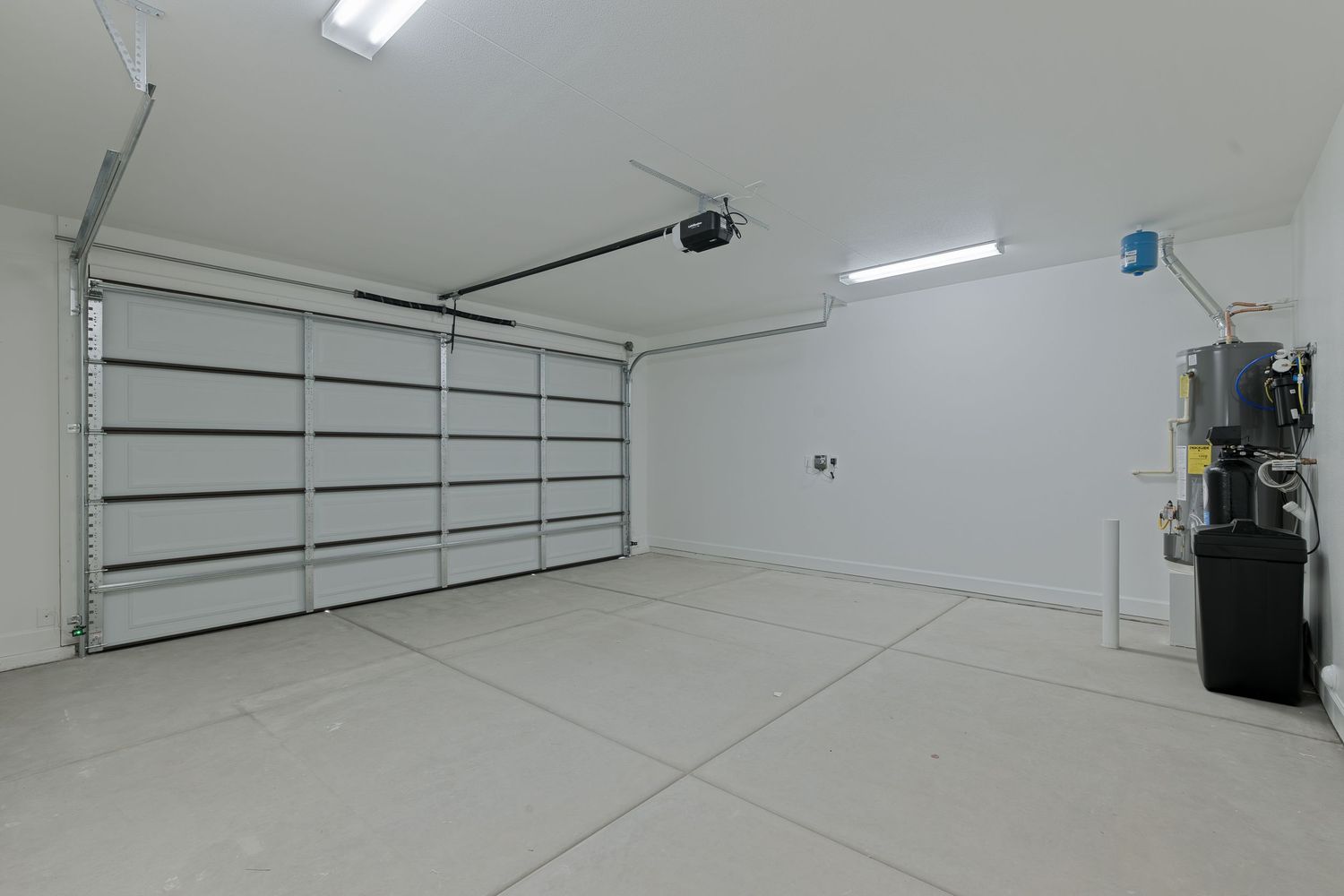 Spacious empty two-car garage with white walls, sectional door, automatic opener, and epoxy concrete floor.