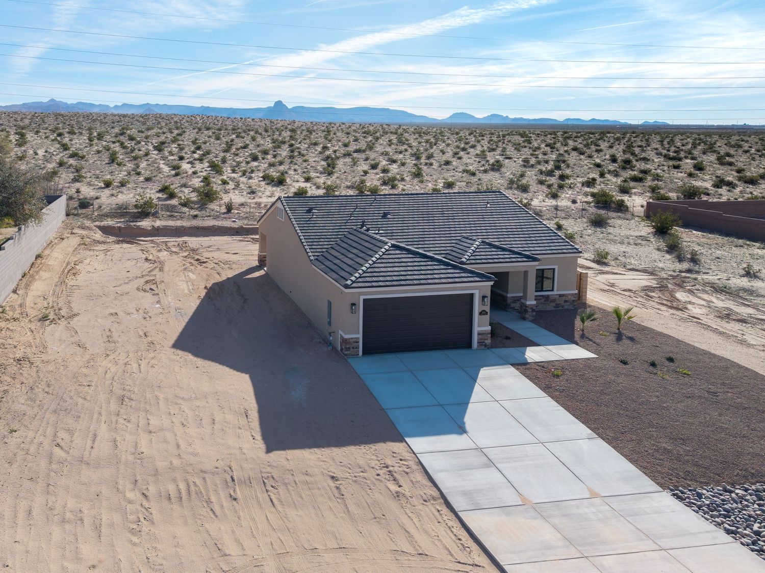 Aerial view of a modern desert home with solar panels and swimming pool surrounded by vast arid landscape.