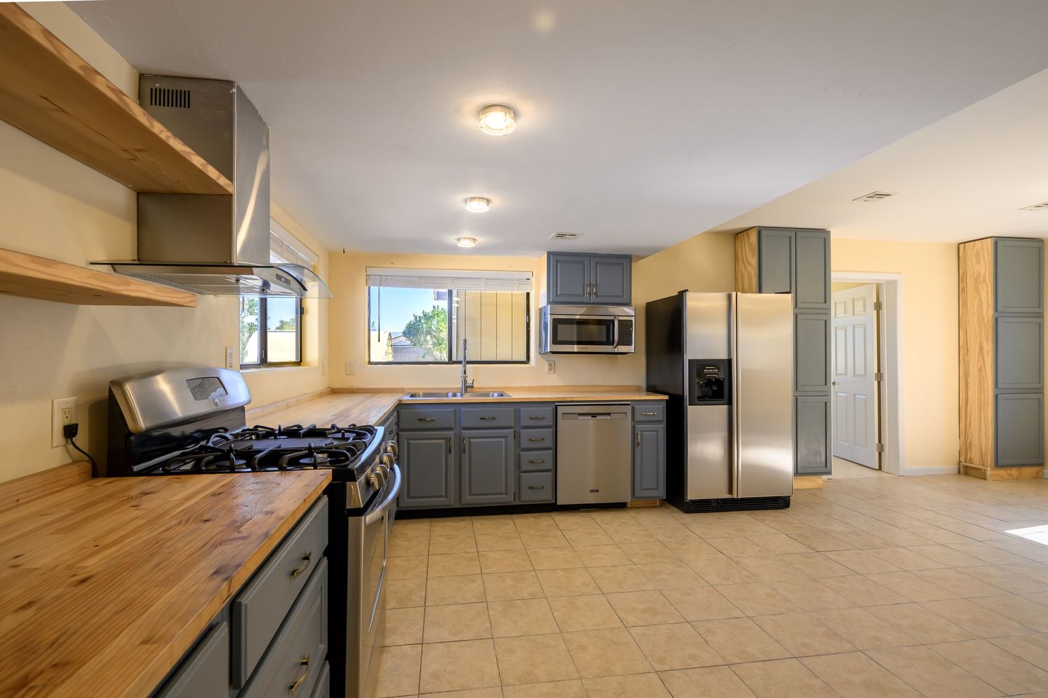 Modern kitchen with gray cabinets, butcher block counters, stainless appliances and tile flooring.