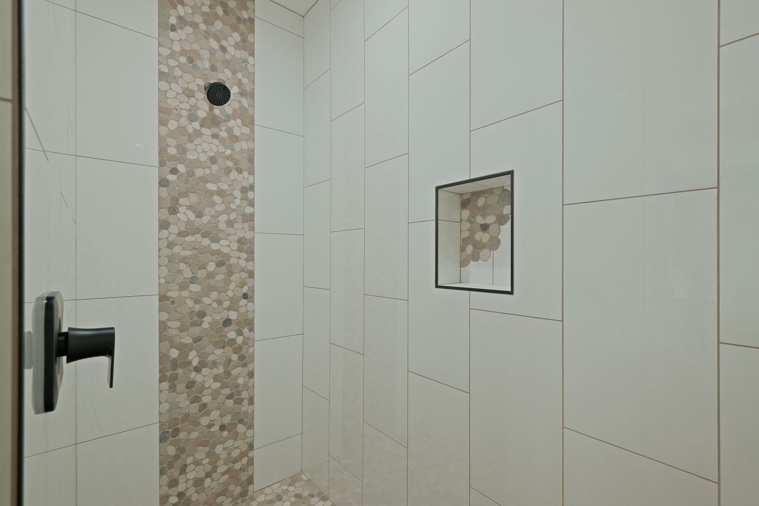 Modern bathroom shower interior with white tile walls and decorative stone accent strip extending vertically.