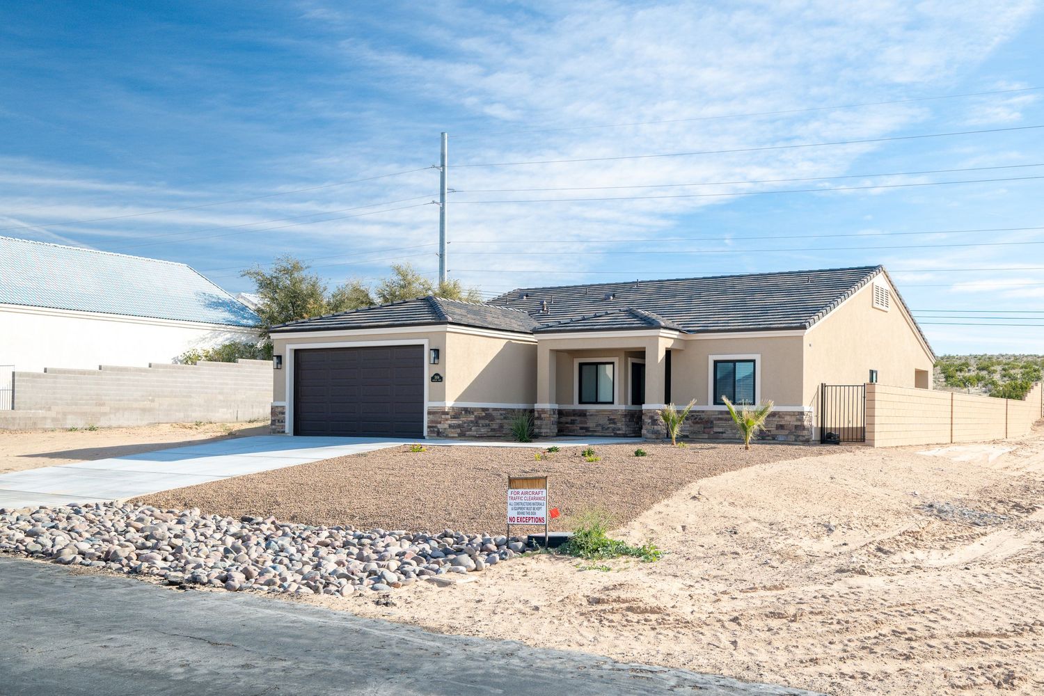 New construction single story ranch home with attached garage and desert landscaping under blue skies.