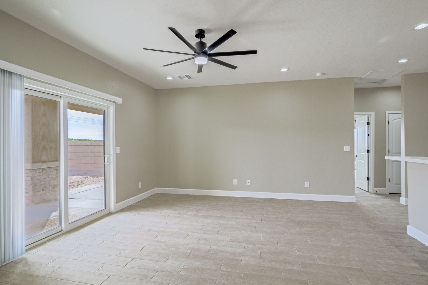 Spacious great room with ceiling fan, large windows, and light gray walls in new construction home.