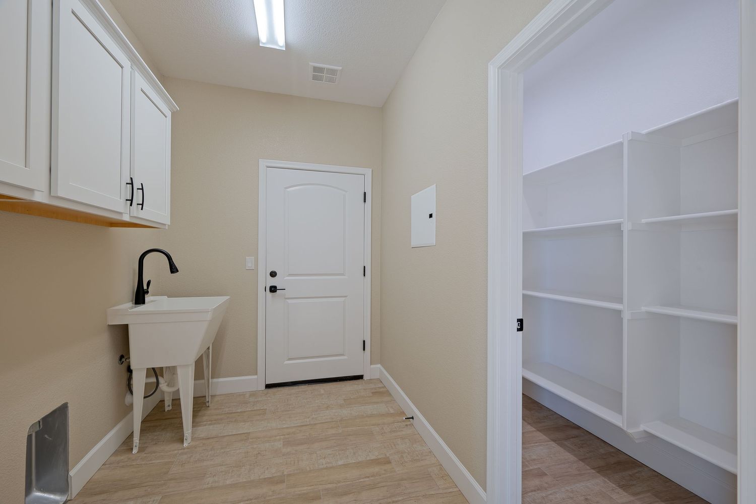 Modern laundry room with white cabinets, utility sink, light wood floors and built-in storage shelves.