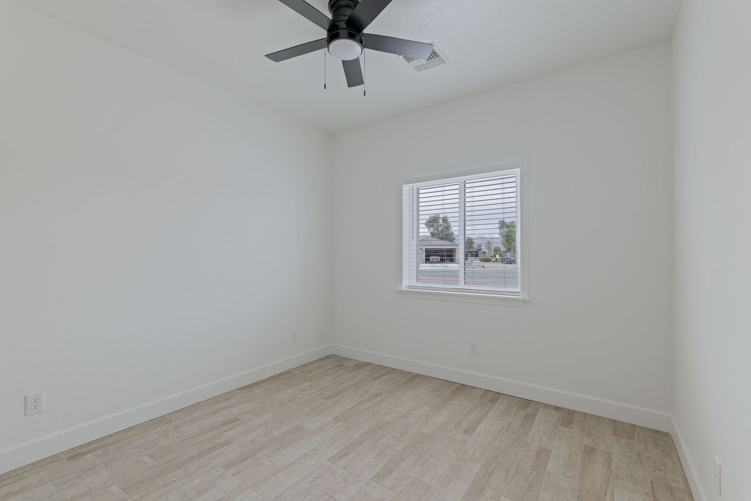 Empty bedroom with light wood floors, white walls, a ceiling fan, and a single window with natural light.