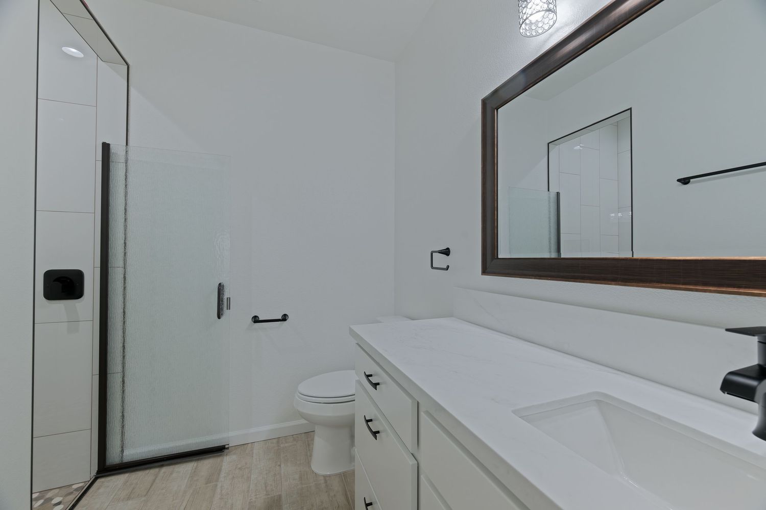 Modern bathroom with white double vanity, large mirror, walk-in shower, and light wood-look tile flooring.
