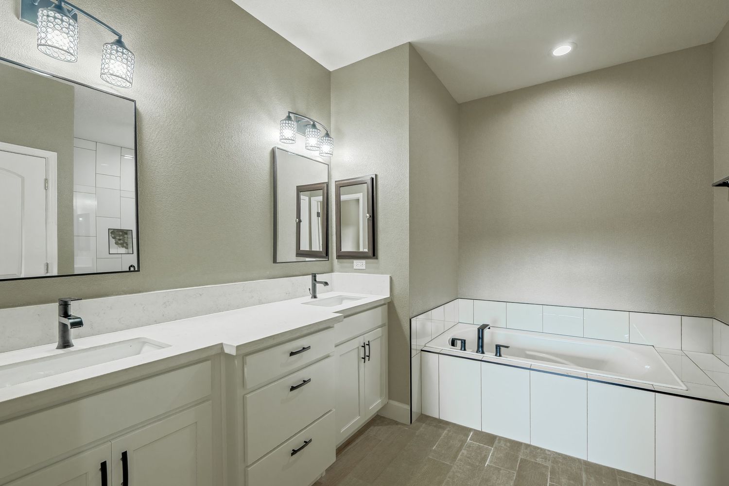 Modern master bathroom with white double vanity, marble countertops, and corner soaking tub in light gray tones.