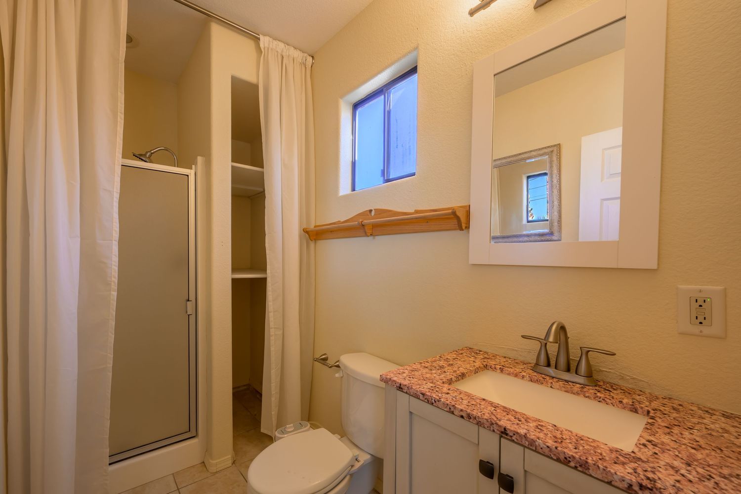 Narrow white hallway with pink granite countertop vanity and mirror showing modern bathroom fixtures and lighting.