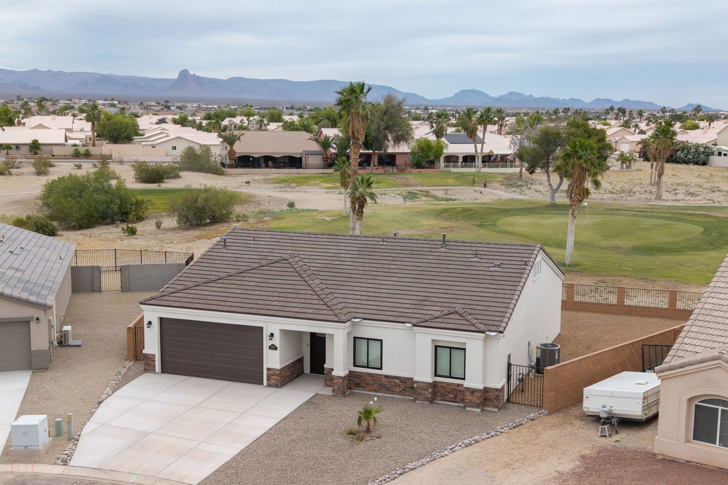 Aerial view of single-story white home with dark roof, two-car garage, and golf course backdrop in Arizona.
