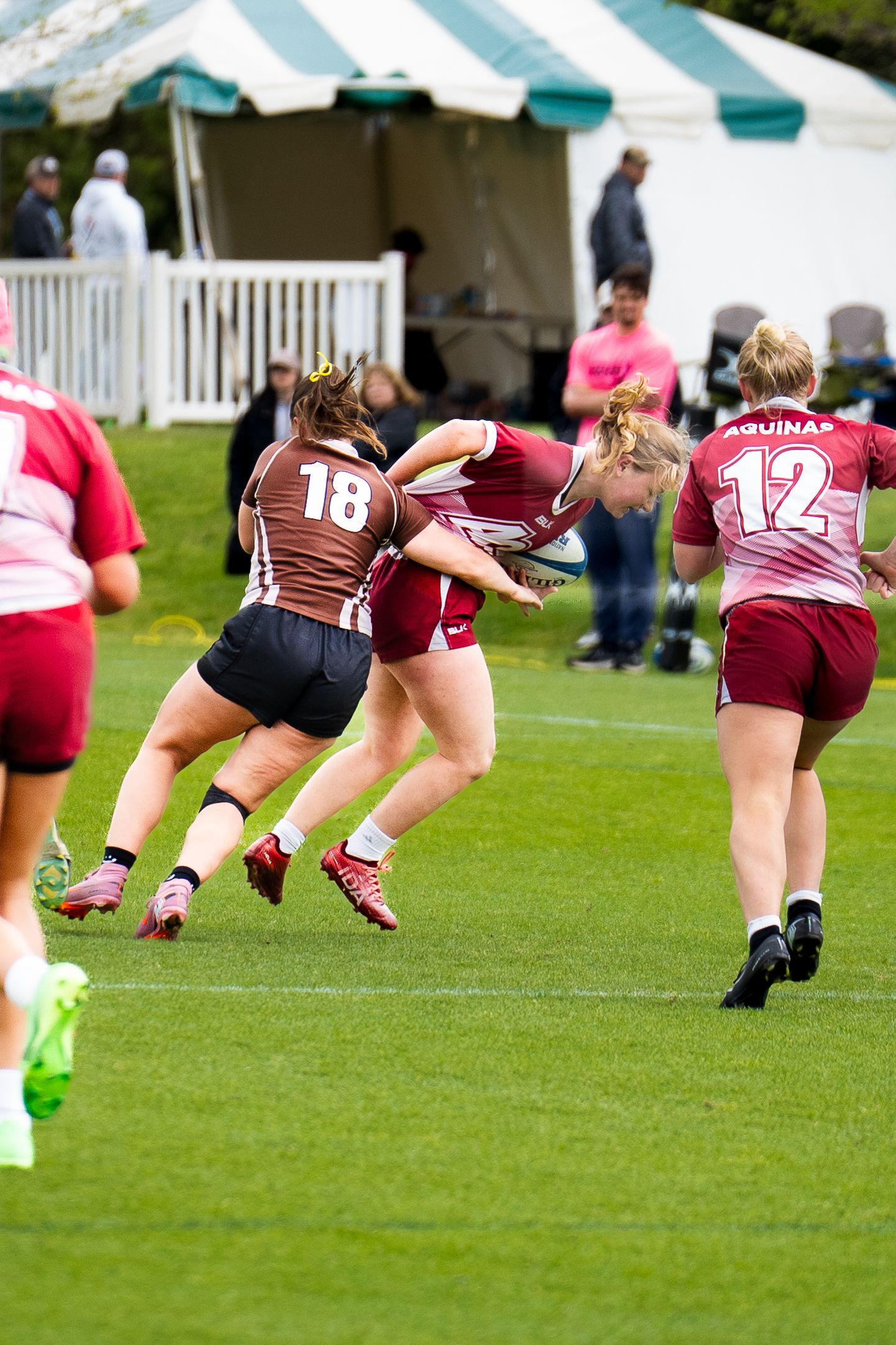 A rugby player wearing number 18 in brown collides with a ball carrier from Aquinas as number 12 runs alongside during a college match.