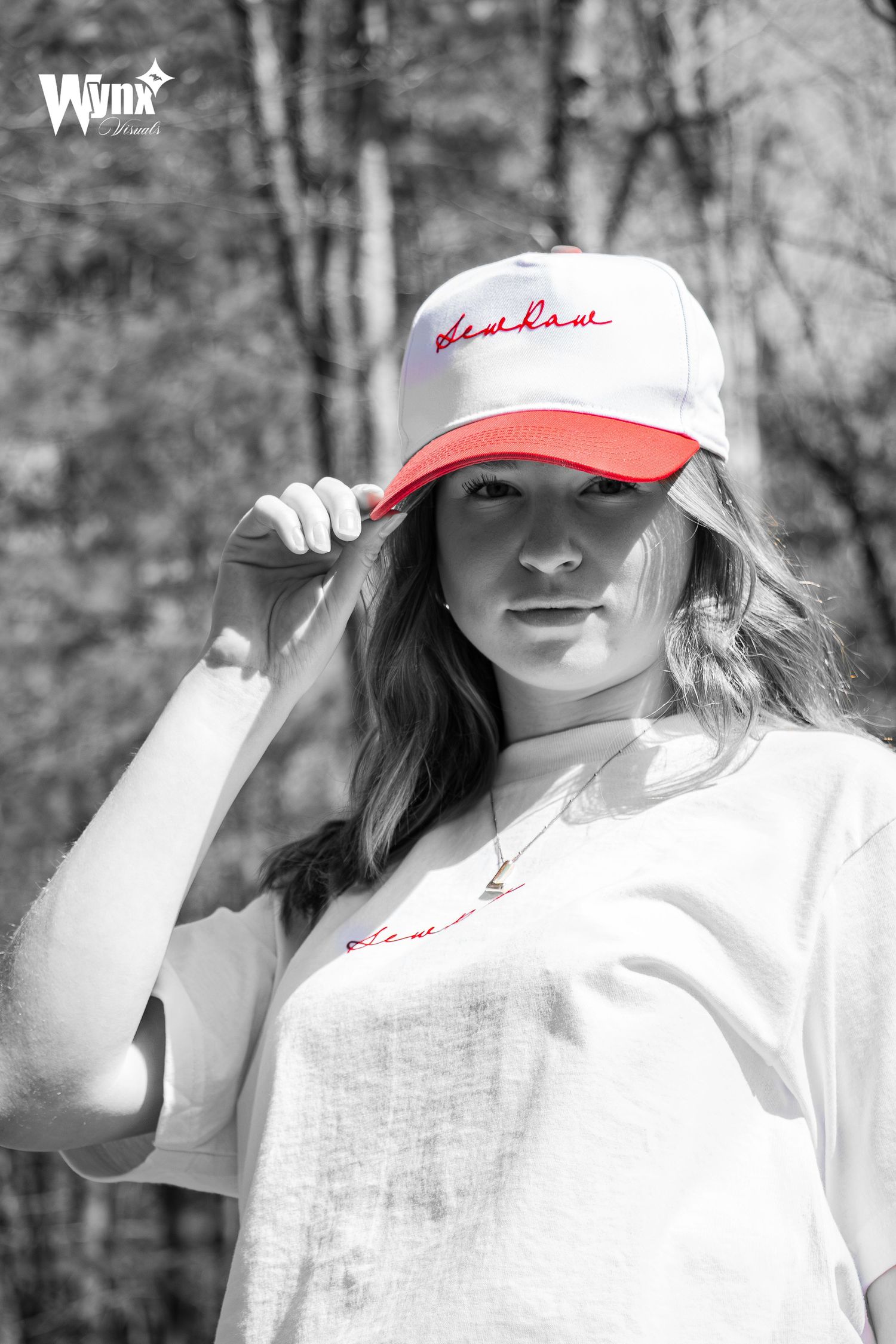 Black and white portrait of a woman touching her Sewlaw cap, with the red cap brim and script highlighted in color.