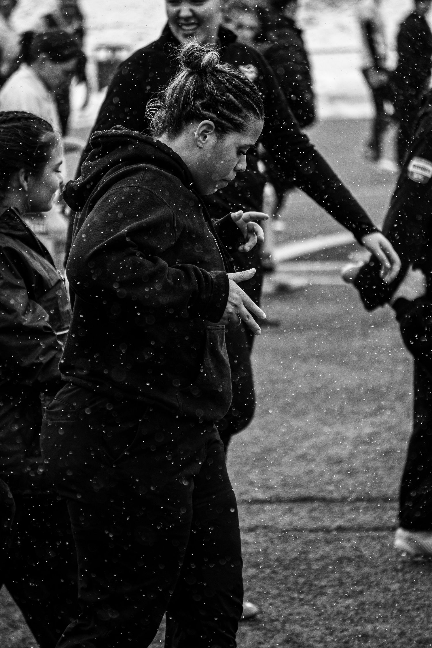 Black and white photo of women in dark hoodies moving together on a field as snow or rain falls during a team warm-up.