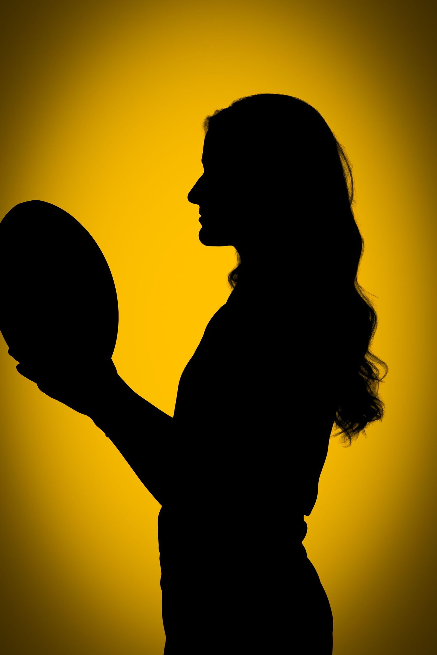 Profile silhouette of a woman with wavy hair holding a rugby ball at her side against a golden yellow glowing background.