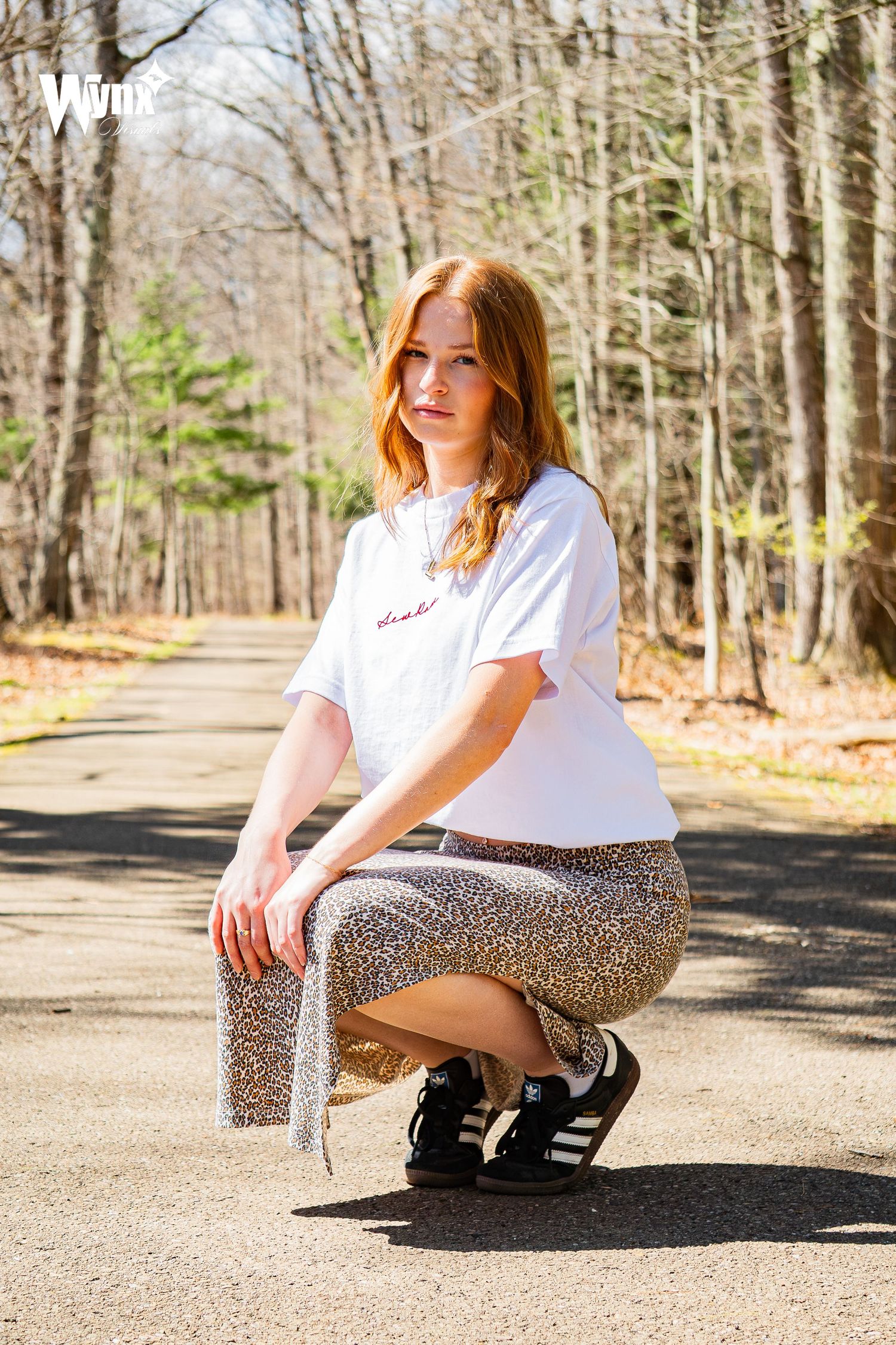 Black and white portrait of a woman in a white and red baseball cap and embroidered tee with red accents in the woods.