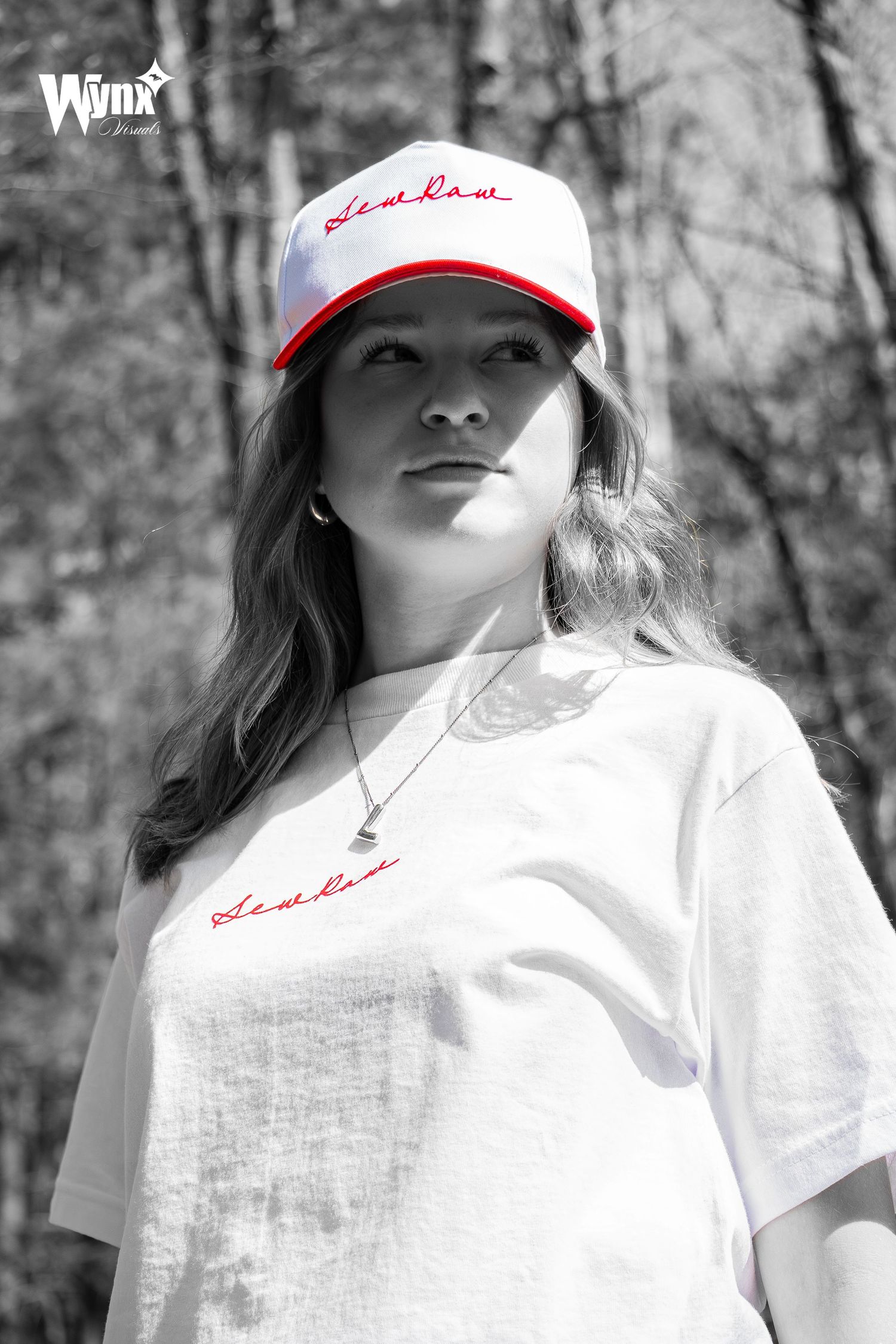 Black and white portrait of a woman in a white Sewlaw tee and red-brim cap, with the red embroidery in selective color.
