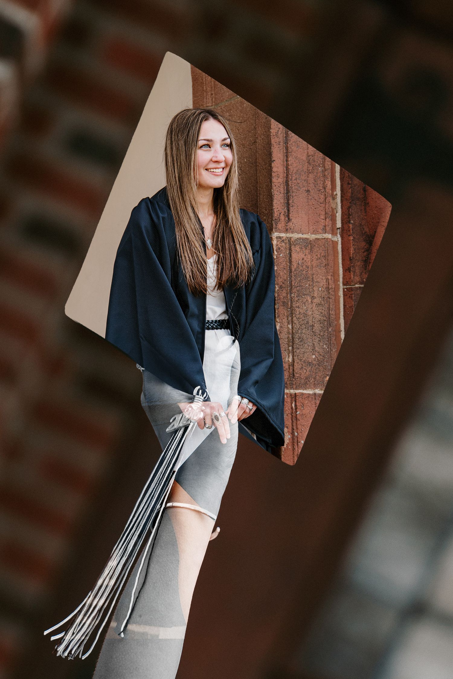 Smiling graduate in a navy gown and tassels stands in a diamond-shaped frame against a brick building backdrop.